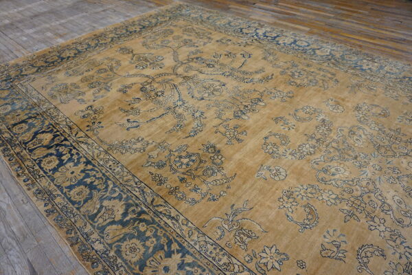 A large, distressed gold rug with elaborate blue and indigo floral patterns rests on weathered wood floors.