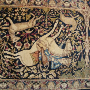 Deep blue rug with a beige hunt scene, surrounded by floral motifs and a detailed border of human faces.