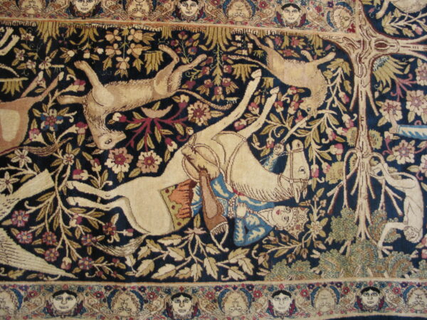 Deep blue rug with a beige hunt scene, surrounded by floral motifs and a detailed border of human faces.