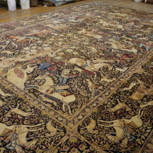 Huge rug featuring complex tan, red, and blue pictorial hunting scenes on a dense black field over wood flooring.