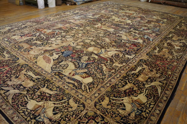 Huge rug featuring complex tan, red, and blue pictorial hunting scenes on a dense black field over wood flooring.