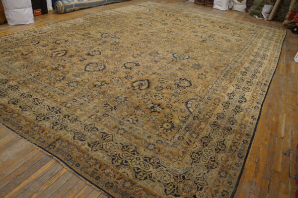 Large traditional gold and navy blue rug with an ornate floral pattern lies on a wooden floor.