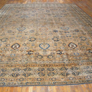 Large traditional tan rug with all-over blue and brown floral patterns on a hardwood floor.