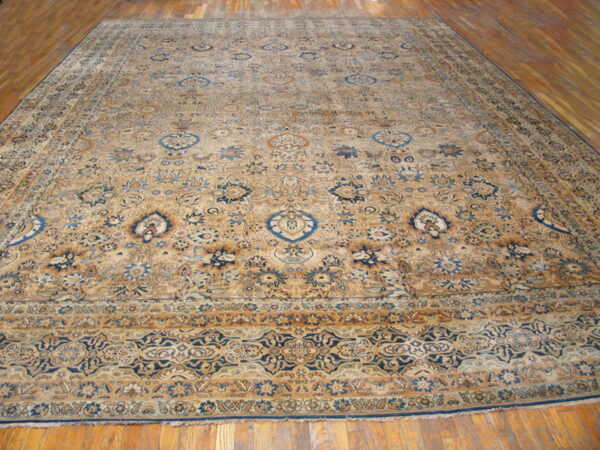 Large traditional tan rug with all-over blue and brown floral patterns on a hardwood floor.