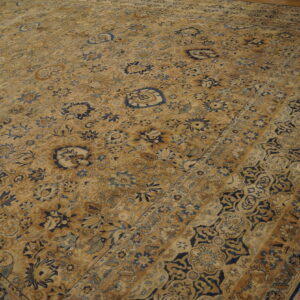 Tan and dark blue traditional rug with a detailed botanical pattern lying on rustic wood planks.