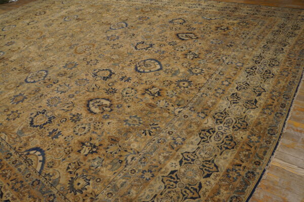 Tan and dark blue traditional rug with a detailed botanical pattern lying on rustic wood planks.