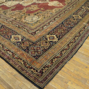 Ornate traditional rug corner in navy, deep red, and gold colors resting on distressed wood planks.