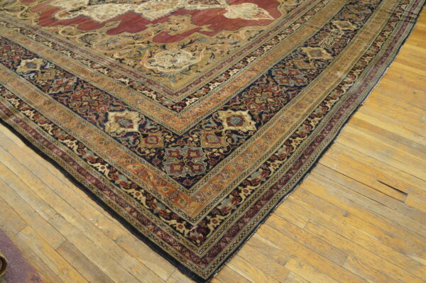 Ornate traditional rug corner in navy, deep red, and gold colors resting on distressed wood planks.