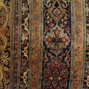 Ornate rug border and field in navy, rust, and gold rests on a yellow hardwood floor.