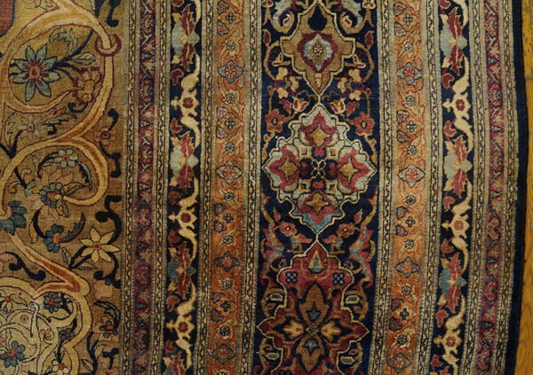 Ornate rug border and field in navy, rust, and gold rests on a yellow hardwood floor.