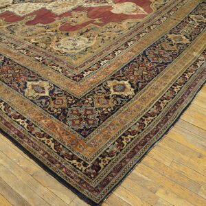 Intricate traditional rug with red, gold, and blue patterns rests diagonally on worn light wood floors.