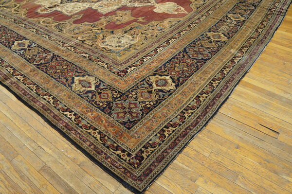 Intricate traditional rug with red, gold, and blue patterns rests diagonally on worn light wood floors.