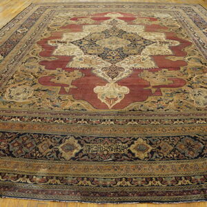 Large traditional red and gold medallion rug with navy borders displayed on light hardwood flooring.