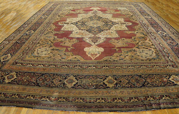 Large traditional red and gold medallion rug with navy borders displayed on light hardwood flooring.