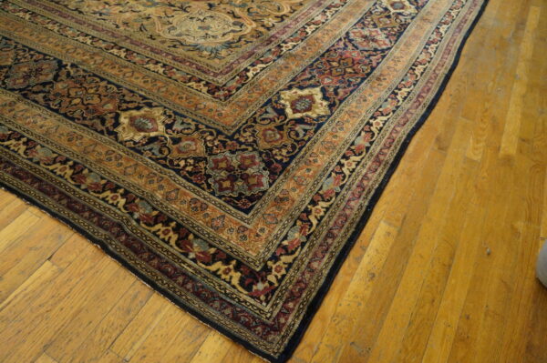 Traditional rug corner displaying detailed navy, gold, and red borders against warm yellow plank flooring.