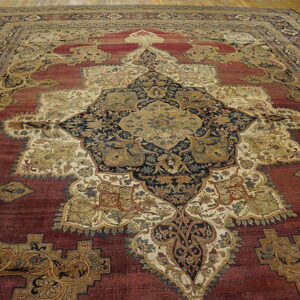 Ornate traditional rug with a central gold and navy medallion on a deep red field over wood flooring.