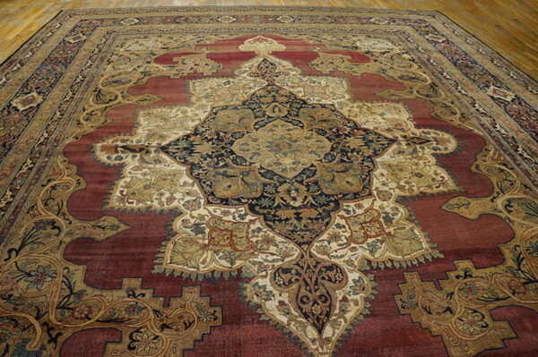 Ornate traditional rug with a central gold and navy medallion on a deep red field over wood flooring.