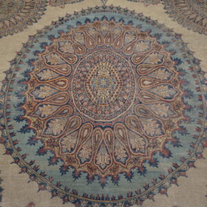Intricate traditional rug pattern featuring a large blue and multicolor central medallion on a light beige field.
