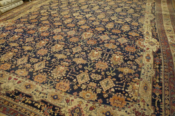 Intricate, large navy rug featuring gold and rust stylized designs and broad multi-layered beige borders.