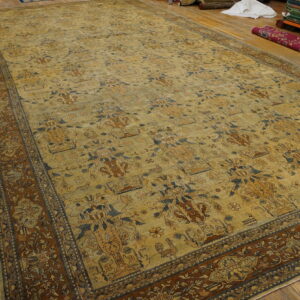 Large low-pile rug with beige field, blue and brown vase motifs, and a rust-toned floral border on wooden flooring.