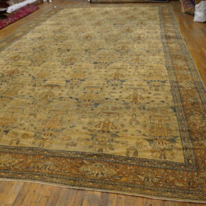 Large golden-tan rug with complex brown and blue patterns displayed on hardwood floor.