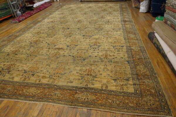 Large golden-tan rug with complex brown and blue patterns displayed on hardwood floor.