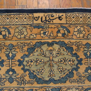 Tan and blue patterned rug detail featuring floral motifs, a geometric border, and script on wooden planks.