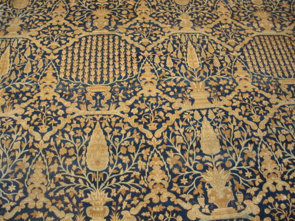Traditional rug features a detailed tan and gold botanical pattern across a dark blue field.