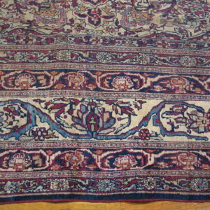 Ornate floral border rug in deep red, navy blue, and beige lying on light hardwood floors.