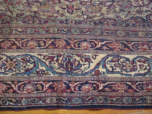 Ornate floral border rug in deep red, navy blue, and beige lying on light hardwood floors.