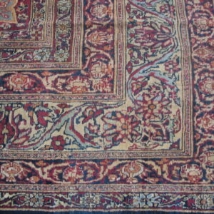 Detailed corner of a traditional rug in red, navy, and tan with complex floral borders and field.