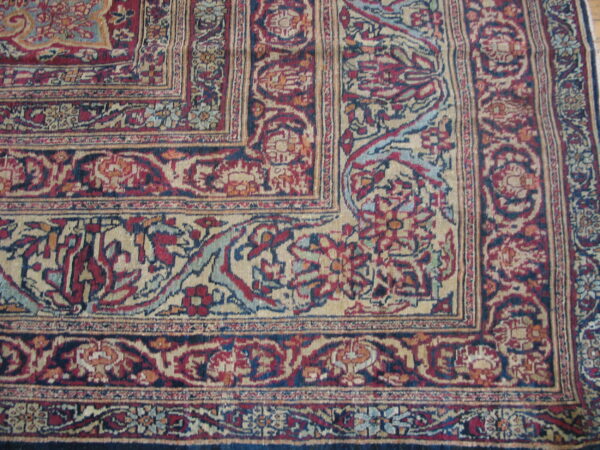 Detailed corner of a traditional rug in red, navy, and tan with complex floral borders and field.