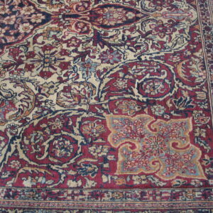Low-pile rug detail showing complex floral motifs in deep reds, indigo, and pale beige.