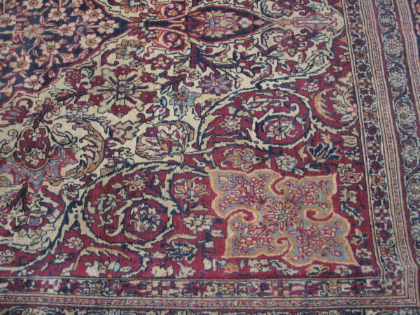 Low-pile rug detail showing complex floral motifs in deep reds, indigo, and pale beige.