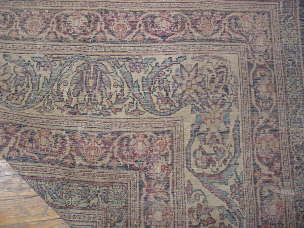 Faded traditional rug with red, blue, and beige floral patterns, peeling back to reveal wood floors.