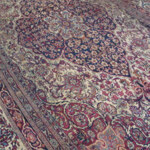 Ornate traditional rug detail showing a navy blue and cream field with crimson, teal, and gold floral patterns.