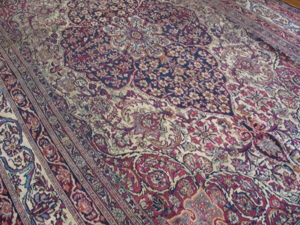 Ornate traditional rug detail showing a navy blue and cream field with crimson, teal, and gold floral patterns.