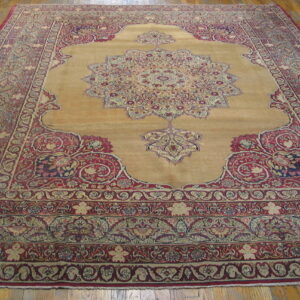Gold and deep red traditional area rug with a detailed medallion lying on wood planks.