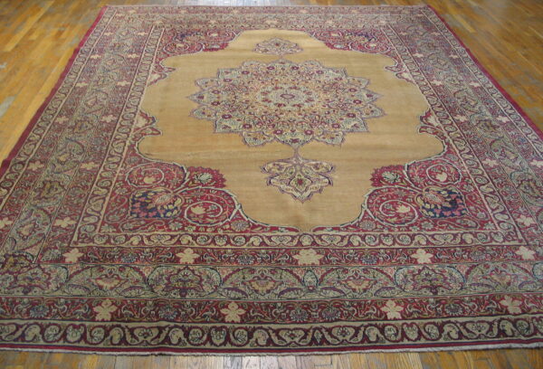 Gold and deep red traditional area rug with a detailed medallion lying on wood planks.