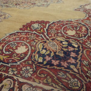Detailed close-up of a rug featuring traditional red, navy, gold, and cream floral designs on a tan ground.