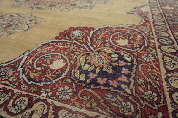 Detailed close-up of a rug featuring traditional red, navy, gold, and cream floral designs on a tan ground.