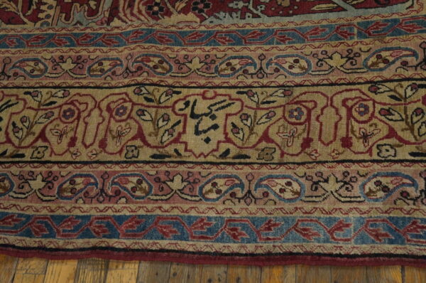 Low pile rug border with intricate tan, red, blue, and pink traditional patterns lying on hardwood flooring.