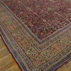 Red rug featuring botanical motifs and a wide beige border is placed on distressed hardwood floor planks.