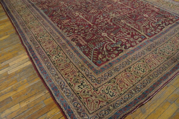 Red rug featuring botanical motifs and a wide beige border is placed on distressed hardwood floor planks.