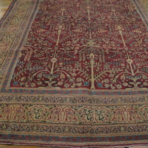 Oversized red rug with Tree of Life pattern and complex beige borders lying on worn wood flooring.