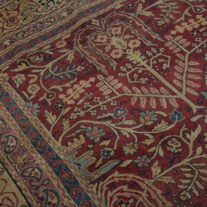 Detailed close-up of a red rug featuring beige, blue, and pink botanical patterns and intricate borders.