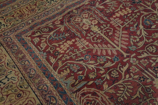Detailed close-up of a red rug featuring beige, blue, and pink botanical patterns and intricate borders.