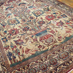 Intricate beige rug featuring a central vase, birds, and dense floral patterns on a wooden floor.