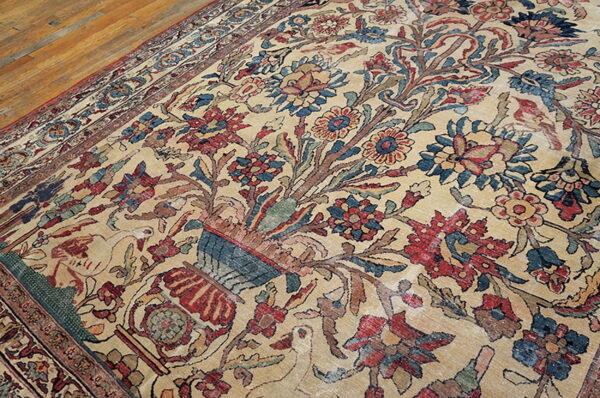 Intricate beige rug with red, blue, and brown floral pattern, including birds, resting on wood floorboards.