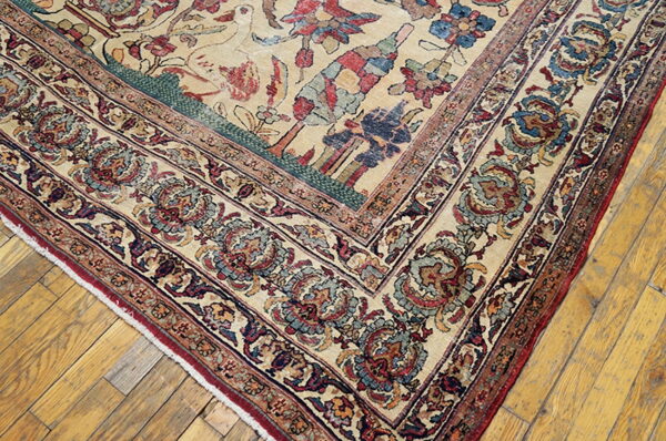 Traditional beige rug with wide floral borders in red and blue, displayed on golden wood planks.